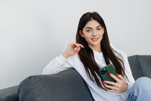 Gelukkige huisvrouw die een mobiele telefoon gebruikt die thuis op een bank zit