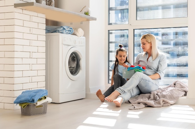 Gelukkige huisvrouw en haar dochter met linnen in de buurt van wasmachine