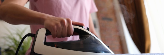 Gelukkige huisvrouw strijkt kleren thuis close-up van elektrisch strijken en vervaagde vrouw in