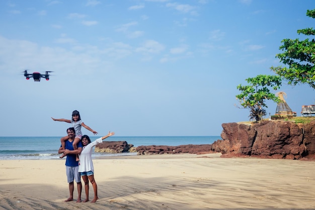 Gelukkige Indiase familie bedient de drone met de afstandsbediening op het strand in Goa