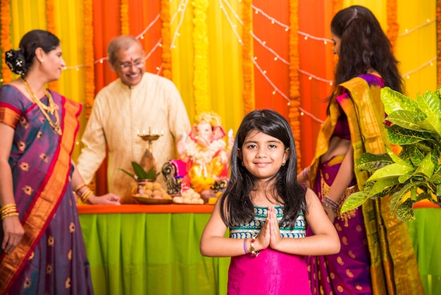 Gelukkige Indiase familie die Ganesh-festival of Chaturthi viert Verwelkoming of het uitvoeren van Pooja en het eten van snoep in traditionele kleding thuis versierd met goudsbloembloemen