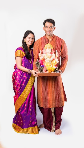 Gelukkige Indiase familie die Ganesh-festival of Chaturthi viert Verwelkoming of het uitvoeren van Pooja en het eten van snoep in traditionele kleding thuis versierd met goudsbloembloemen