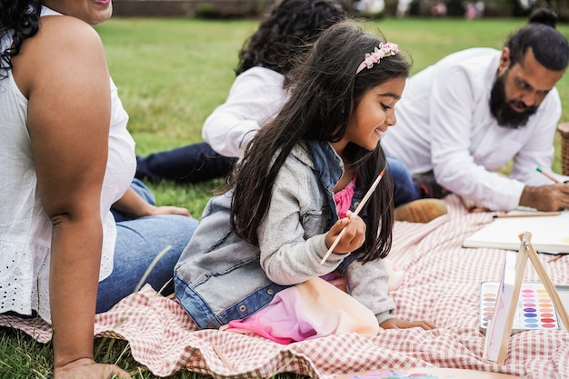 Gelukkige Indiase familie die plezier heeft met schilderen met kinderen buiten in het stadspark - Hoofdfocus op meisjesgezicht