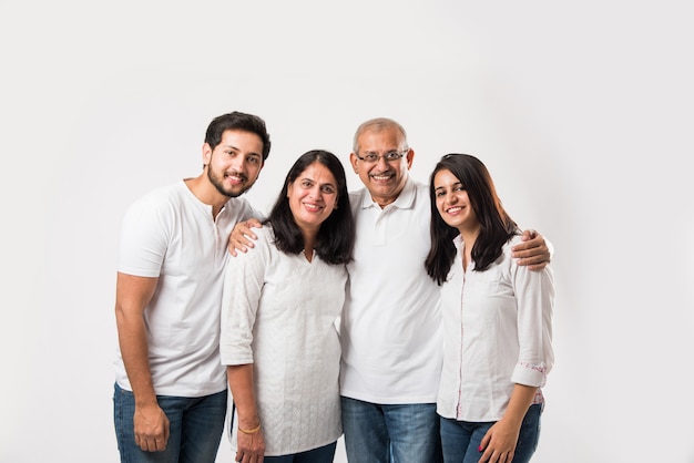 Gelukkige Indiase familie permanent geïsoleerd op witte achtergrond. senior ouders met jonge kinderen die een witte top en een blauwe spijkerbroek dragen. selectieve focus