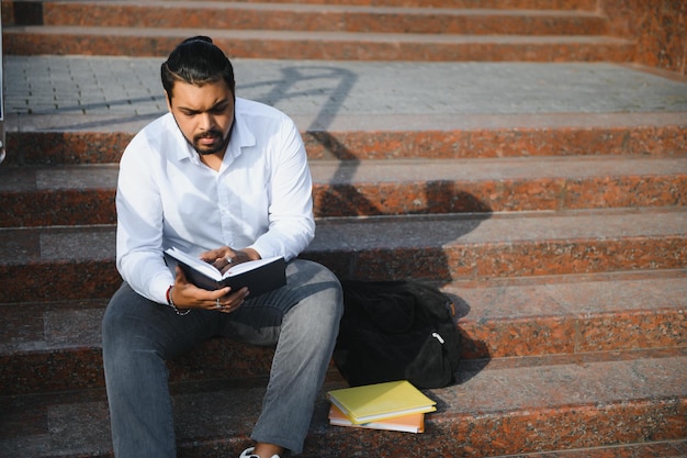 Gelukkige Indiase student zittend op de trap op de universiteitscampus