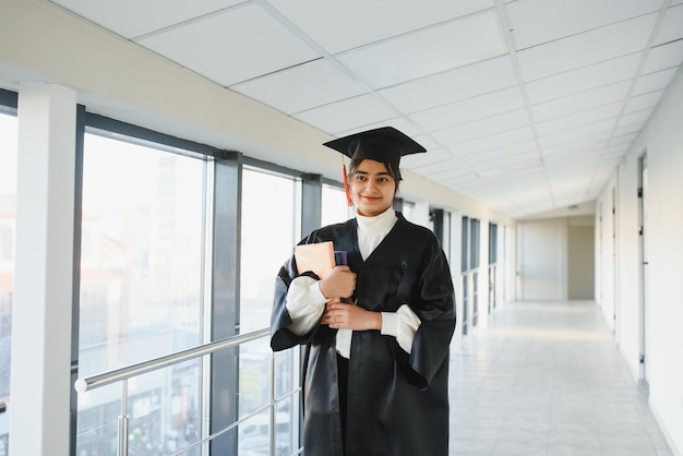 Gelukkige Indiase universiteitsstudent in afstudeerjurk en pet met diplomacertificaat.