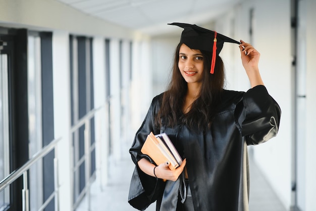 Gelukkige Indiase universiteitsstudent in afstudeerjurk en pet met diplomacertificaat.