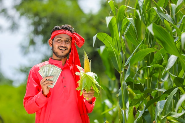 Gelukkige Indische landbouwer die graanfruit en Indische munt toont bij groen maïsveld