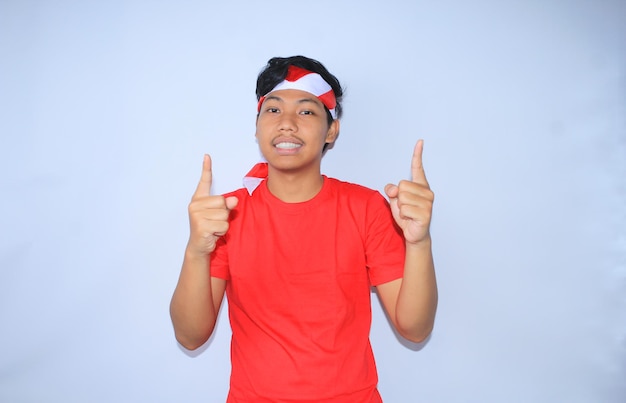 Gelukkige indonesische jonge man glimlacht en wijst met de vinger naar het presenteren van een product met een rood t-shirt
