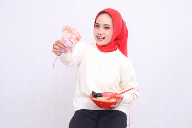 Gelukkige Indonesische vrouw in hijab met rupiah geld en een kom met ramen Chinees eten amp chops