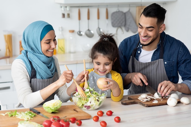 Gelukkige islamitische familie met dochtertje samen eten bereiden in de keuken, ouders uit het Midden-Oosten en schattig vrouwelijk kind die een gezonde salade maken voor ontbijt of lunch, genietend van thuis koken