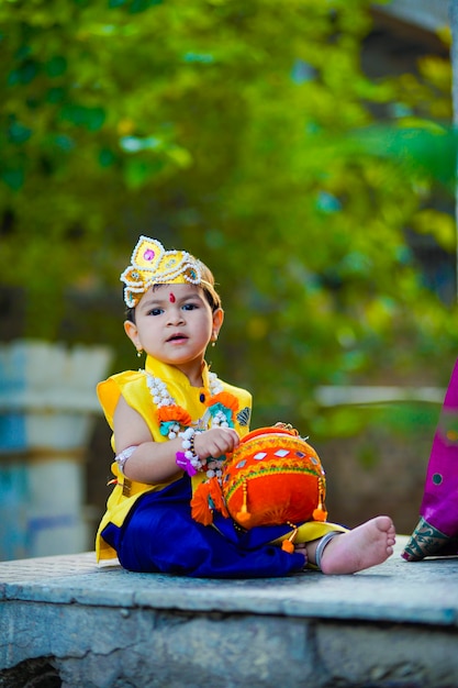 Gelukkige Janmashtami-wenskaart met kleine Indiase jongen die zich voordeed als Shri krishna of kanha/kanhaiya met Dahi Handi-afbeelding en kleurrijke bloemen.
