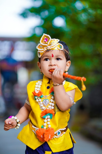 Gelukkige Janmashtami-wenskaart met kleine Indiase jongen die zich voordeed als Shri krishna of kanha/kanhaiya met Dahi Handi-afbeelding en kleurrijke bloemen.