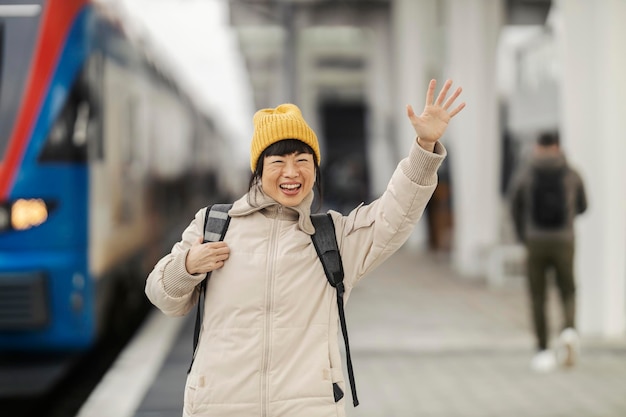 Foto gelukkige japanse reiziger staat op het treinstation en zwaait naar een vriend