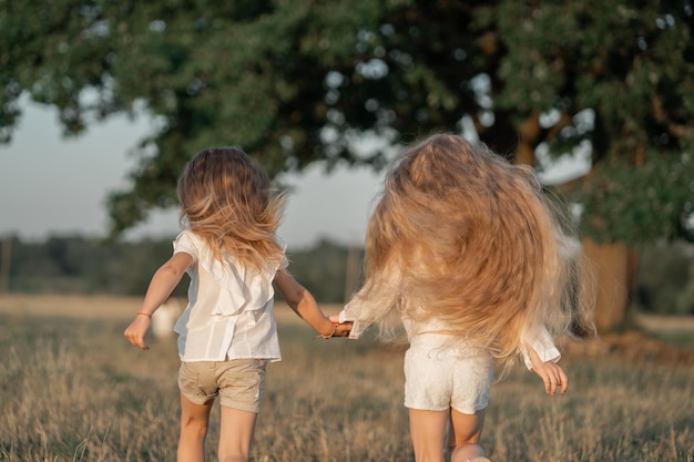 Foto gelukkige jeugd in het dorp twee blonde meisjes rennen het veld in de zussen houden elkaar vast en rennen