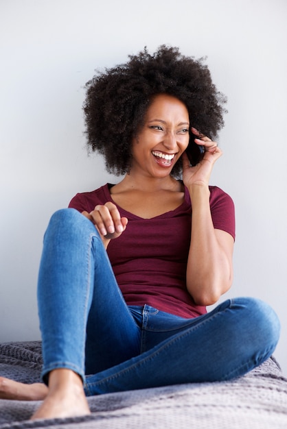 Gelukkige jonge Afrikaanse vrouw die en op mobiele telefoon ontspant spreekt