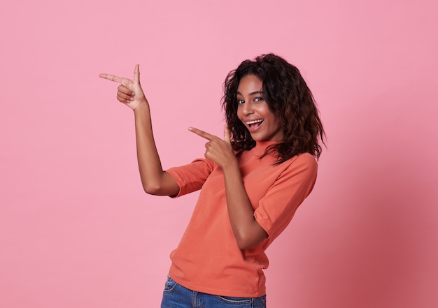 Gelukkige jonge Afrikaanse vrouw die zich met haar vinger richten bevinden geïsoleerd over roze met exemplaarruimte.