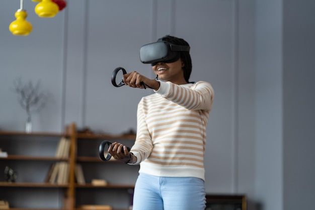 Gelukkige jonge afro-amerikaanse vrouw die een virtual reality-bril draagt die thuis videogames speelt