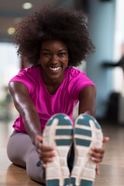 gelukkige jonge Afro-Amerikaanse vrouw in een sportschool die zich uitstrekt en opwarmt voor de training