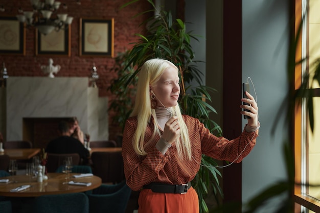 Gelukkige jonge albinovrouw die met oortelefoons het telefoonscherm bekijken
