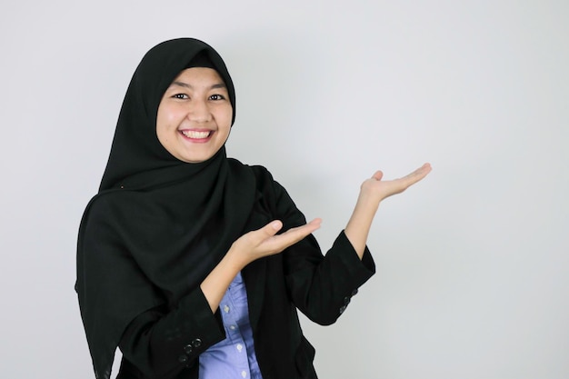 Gelukkige jonge Aziatische islamvrouw die een hoofddoek draagt, glimlacht en wijst ernaast