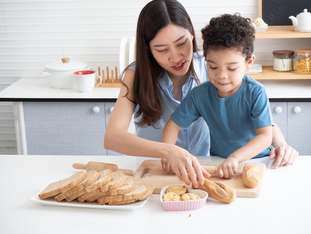 Gelukkige jonge Aziatische moeder kust haar schattige zoontje op de wang terwijl ze thuis koekjes maakt in de keuken Grappig educatief voor kinderen conceptxA