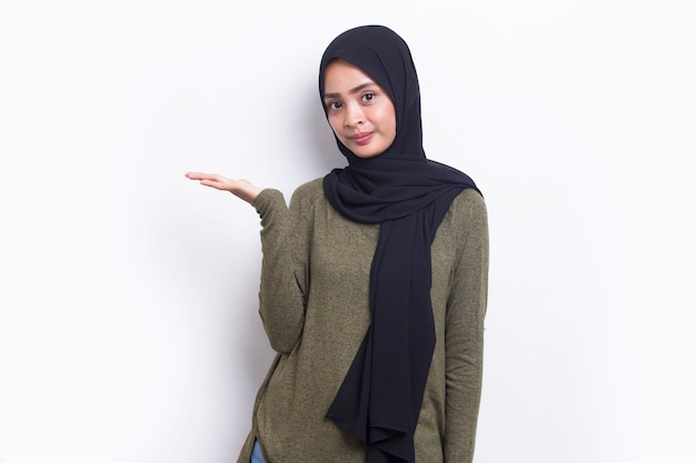 Gelukkige jonge Aziatische moslimvrouw die met vingers naar verschillende richtingen wijst die op wit worden geïsoleerd