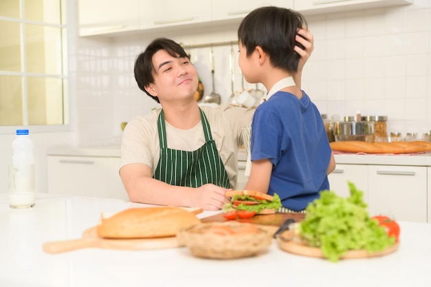 Gelukkige jonge Aziatische vader die thuis steun geeft aan zijn zoon in de keuken