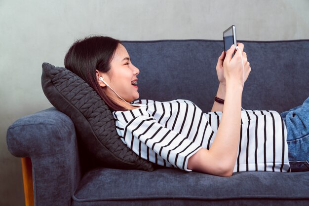 Gelukkige jonge Aziatische vrouw die een digitale tablet houden en online sociale levensstijl op bank in het huis gebruiken.