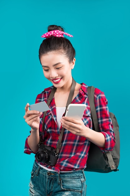 Gelukkige jonge aziatische vrouw met creditcard en smartphone die zich over blauw bevindt.