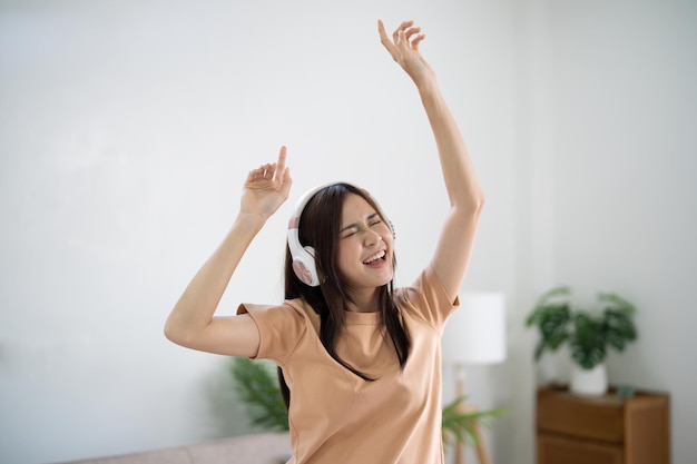 Gelukkige jonge Aziatische vrouw met koptelefoon veel plezier en dansen luisteren naar muziek ontspannen in de woonkamer mooie vrolijke vrouw dansen in huis