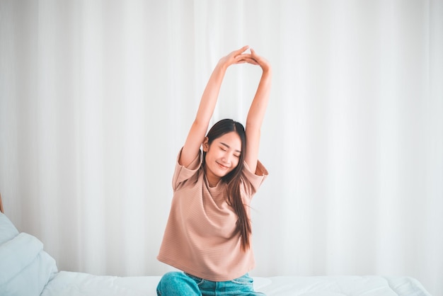 Gelukkige jonge aziatische vrouwen die zich uitstrekken en 's ochtends thuis in haar slaapkamer wakker worden
