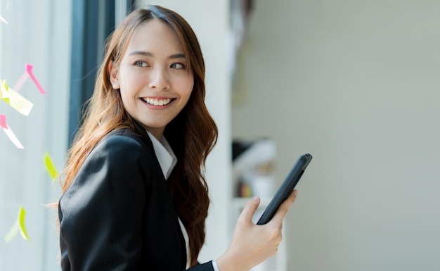 Gelukkige jonge Aziatische zakenvrouw die een pak draagt met een mobiele telefoon