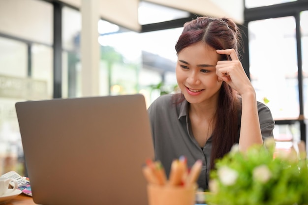 Gelukkige jonge Aziatische zakenvrouw die op kantoor werkt met een draagbare laptopcomputer