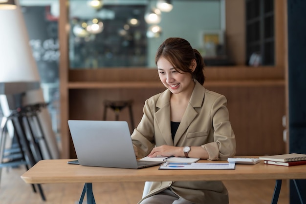 Gelukkige jonge Aziatische zakenvrouw die werkt met een laptopcomputer op kantoor