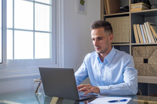 Foto gelukkige jonge blanke millennial zakenman die thuis aan het bureau werkt met een laptop of computer die plezier heeft jonge mannelijke persoon in videoconferentie die zich bezighoudt met het bedrijf of de markt