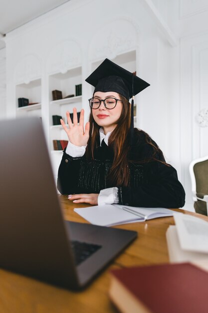 Gelukkige jonge blanke vrouw die universiteitsafstuderen viert tijdens een videogesprek met vriend of familie.