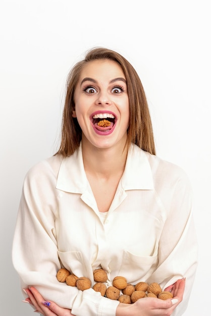 Gelukkige jonge blanke vrouw die walnoten eet met een open mond op een witte achtergrond met kopieerruimte