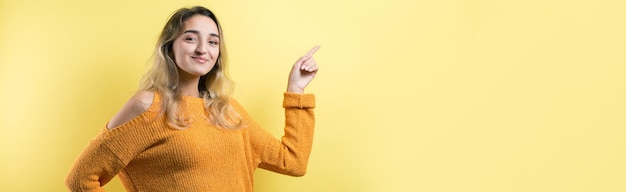 Gelukkige jonge blanke vrouw in een gele trui die met de vingers wegwijst.