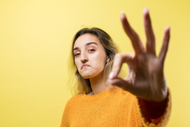 Gelukkige jonge blanke vrouw in een oranje trui die duim omhoog maakt en glimlacht Goed gedaan en respect