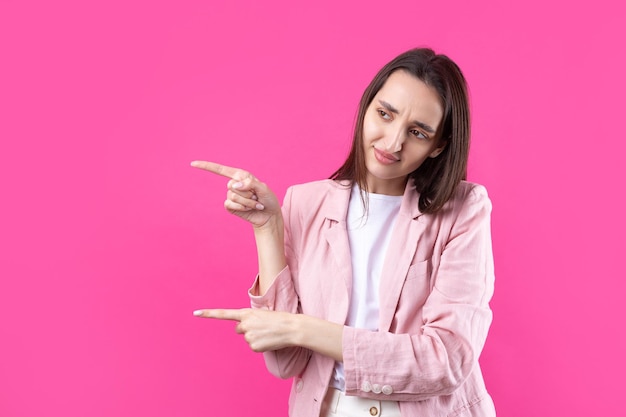 Gelukkige jonge blanke vrouw in een roze jas die met de vingers wegwijst