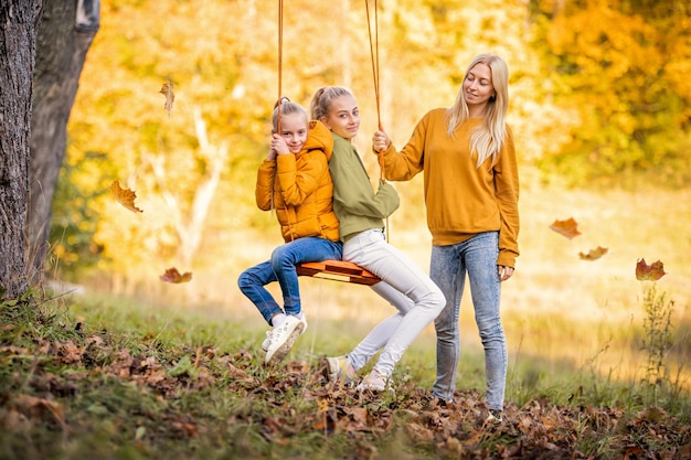 Gelukkige jonge blonde moeder met los haar schudt haar dochter op een schommel op een touwschommel in de herfst in het park