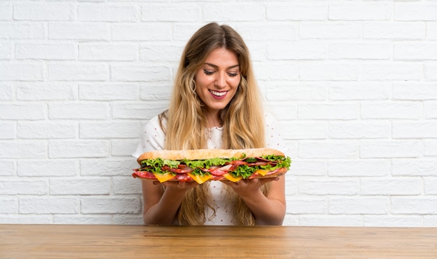 Gelukkige Jonge blonde vrouw die een grote sandwich houdt