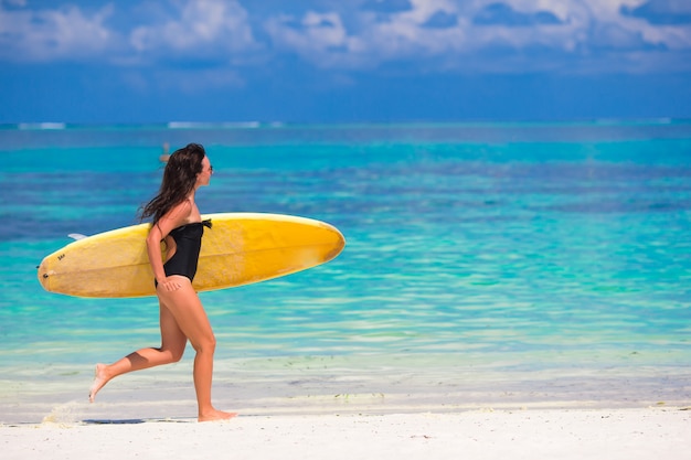 Gelukkige jonge brandingsvrouw die bij het strand met een surfplank loopt