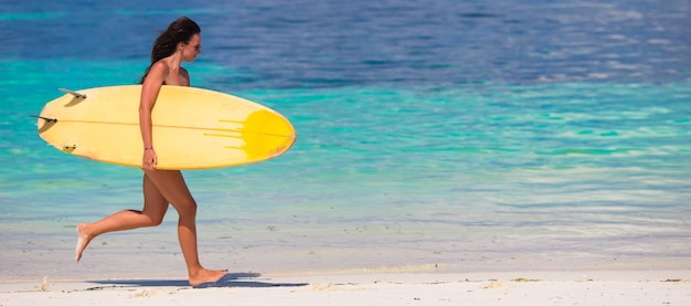 Gelukkige jonge brandingsvrouw die bij het strand met een surfplank loopt