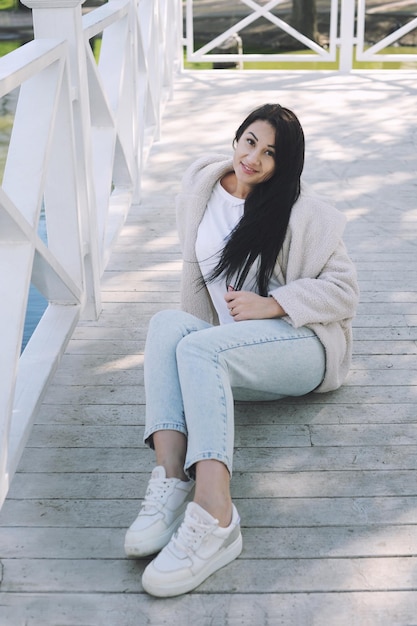 Gelukkige jonge brunette vrouw buiten gekleed in faux witte bontjas en jeans