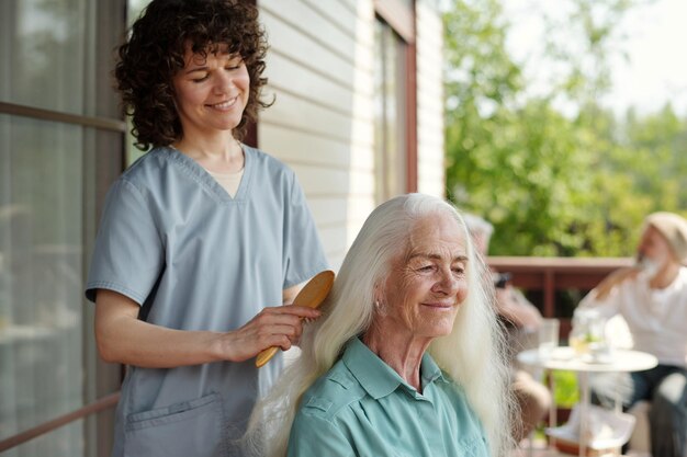 Foto gelukkige jonge brunette vrouw die het lange haar van een oudere vrouwelijke patiënt borstelt