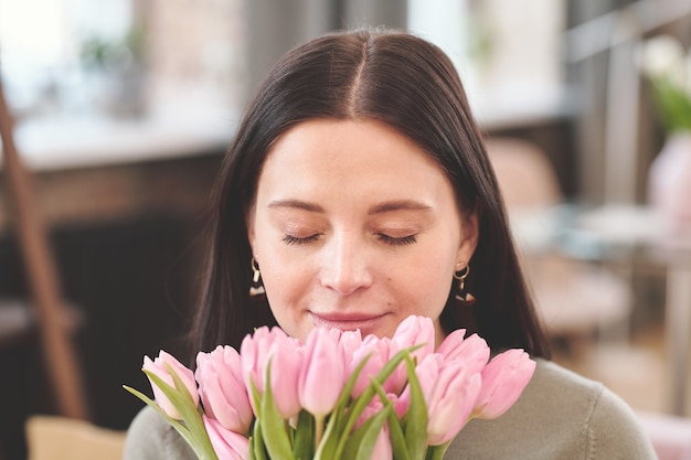 Gelukkige jonge brunette vrouw ruikende bos roze tulpen