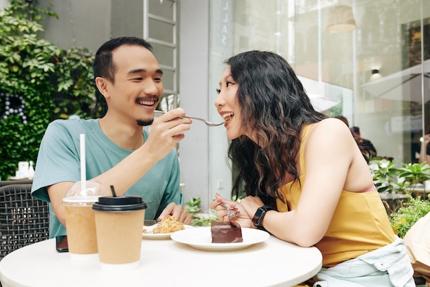 Gelukkige jonge Chinese man die vriendin voedt met een fluitje van een cent als ze aan de cafétafel zitten
