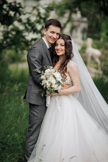 Gelukkige jonge echtpaar Bruiloftsportret De bruid knuffelde de bruidegom teder Jonge bruiden en bruidegomen omhelzen elkaar teder terwijl ze naar de camera kijken Bruiloftsboeket Lente bruiloft